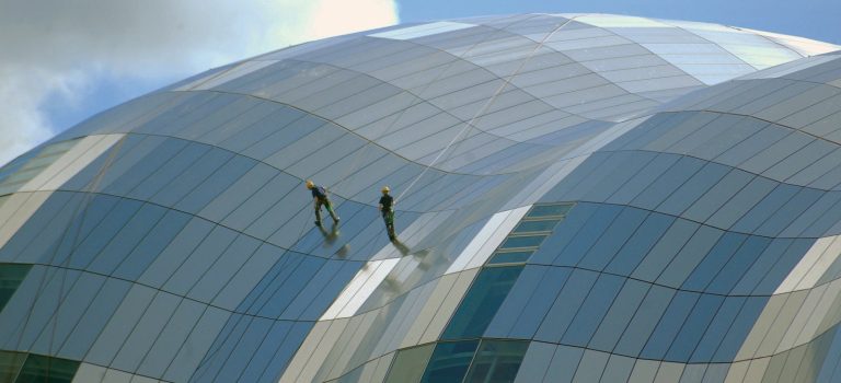 two person standing on glass-panel building under cloudy sky